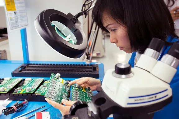 A person inspecting a PCB using a microscope or testing equipment.