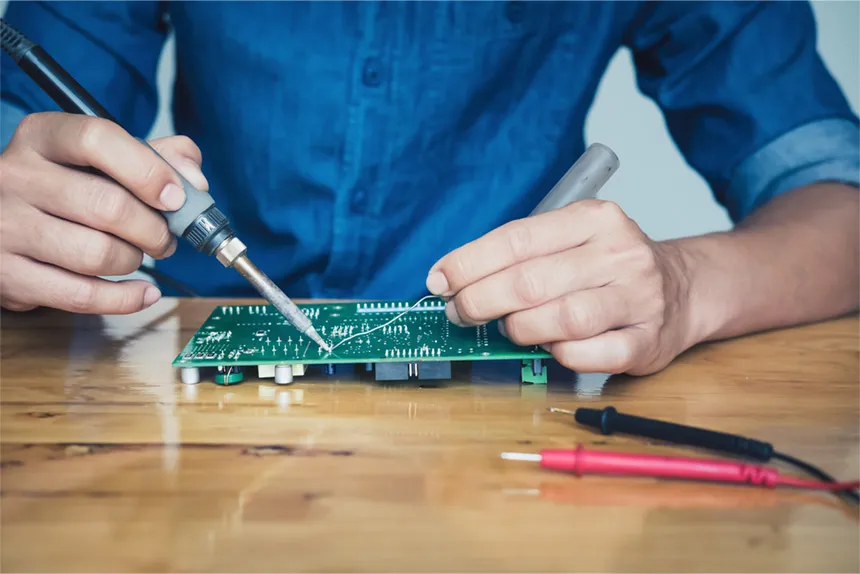 A person manually soldering components onto a PCB board.