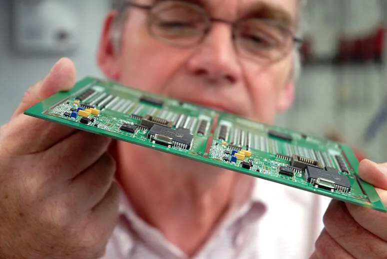 A worker inspecting PCBs for defects under magnification.