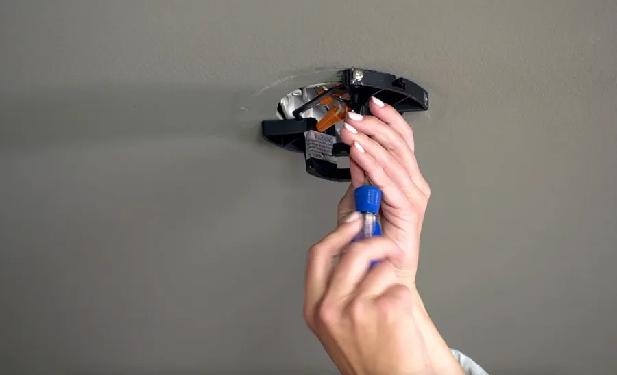 Hands installing a new fan capacitor into a ceiling fan.