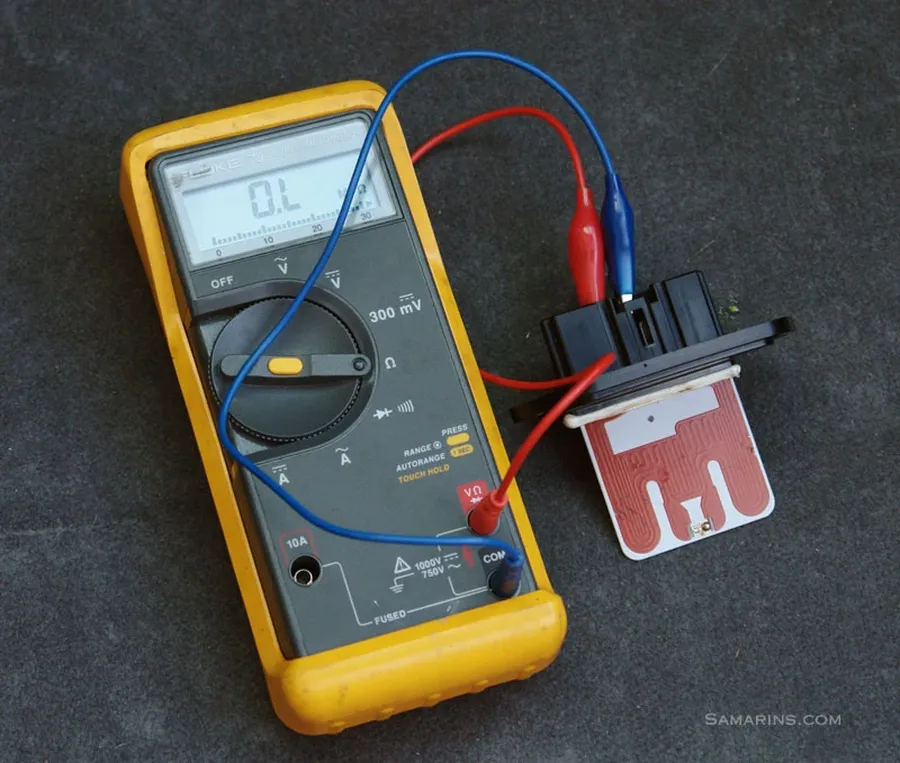 A technician using a multimeter to diagnose an AC resistor in a car.