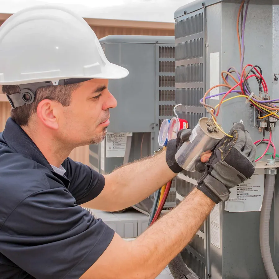 A person replacing a capacitor in an air conditioning unit.