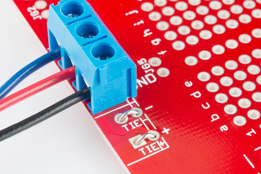 A detailed view of the holes and copper pads on a solderable breadboard.